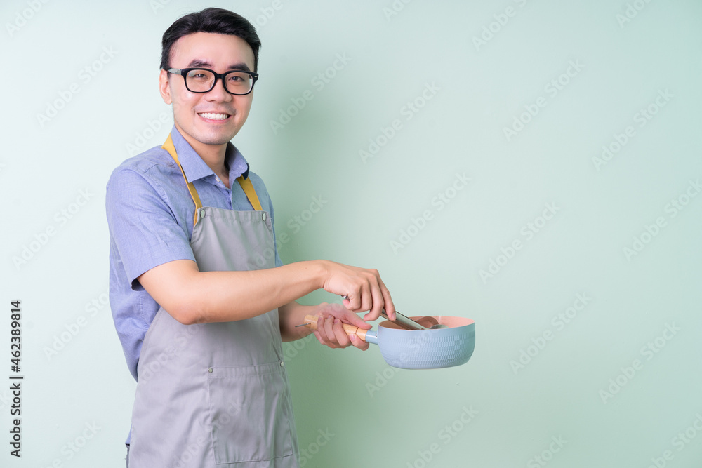 Young Asian man wearing apron posing on green background