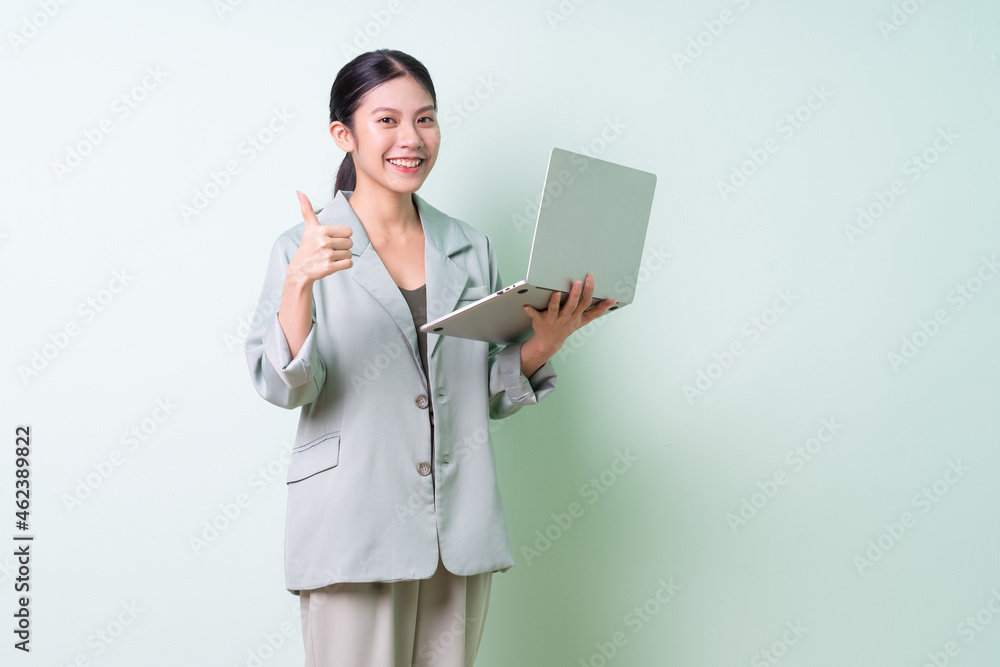 Young Asian businesswoman holding laptop on green background