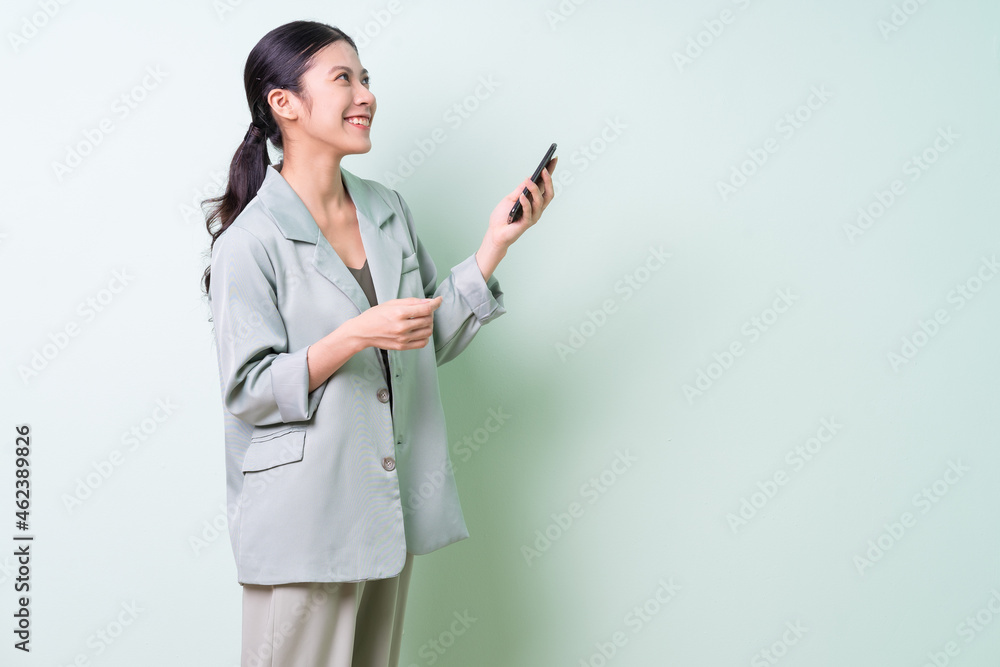 Young Asian businesswoman holding smartphone on green background