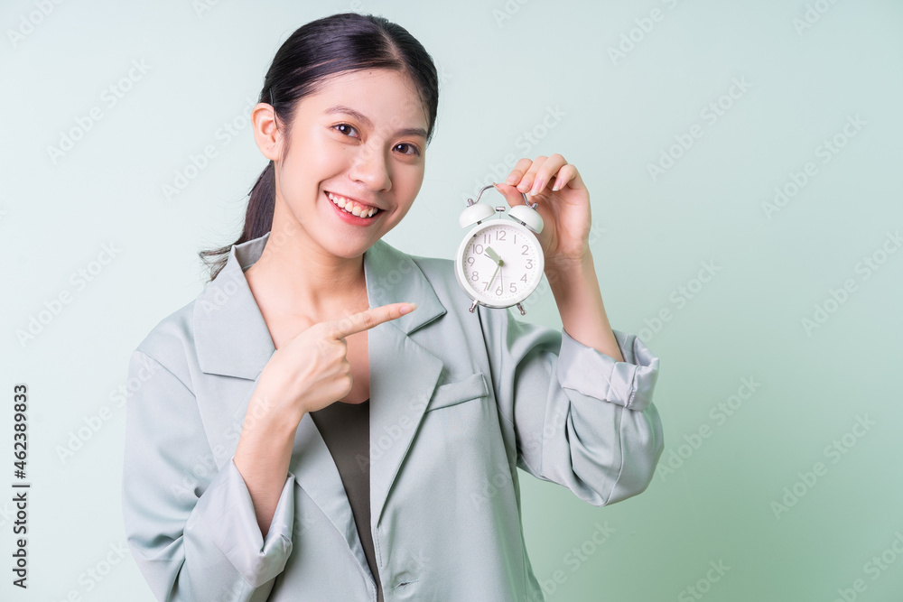 Young Asian businesswoman holding clock on green background