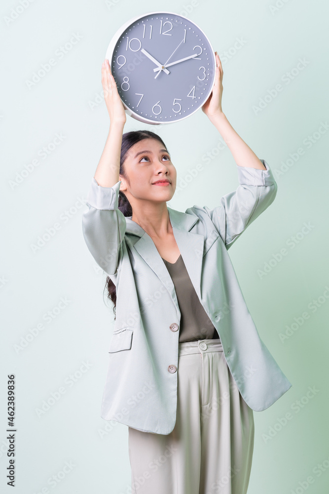 Young Asian businesswoman holding clock on green background