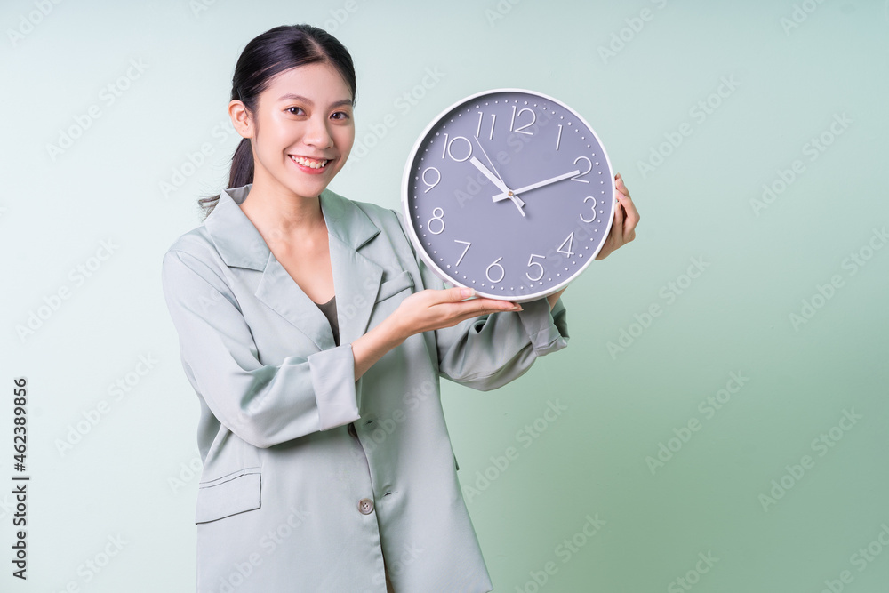 Young Asian businesswoman holding clock on green background