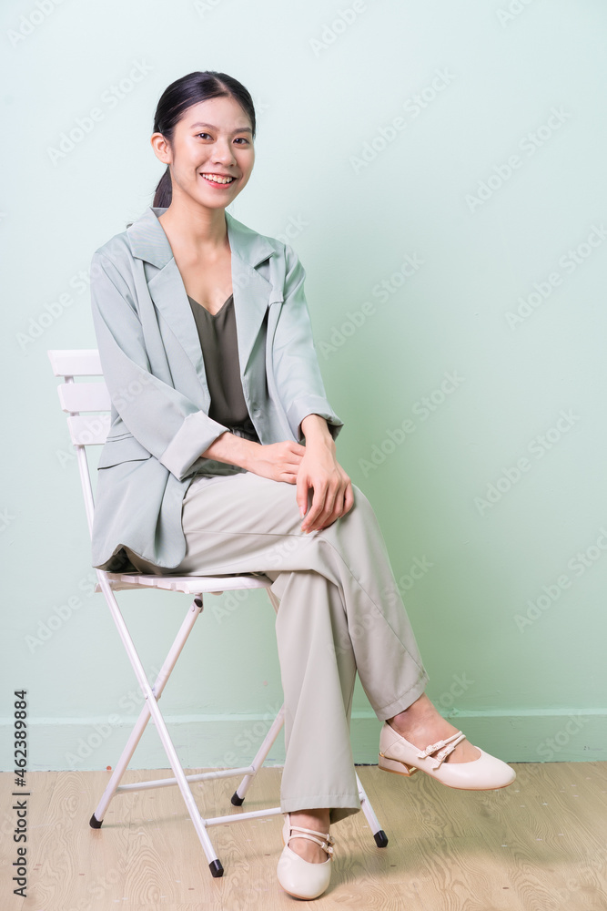 Young Asian businesswoman sitting on chair on green background