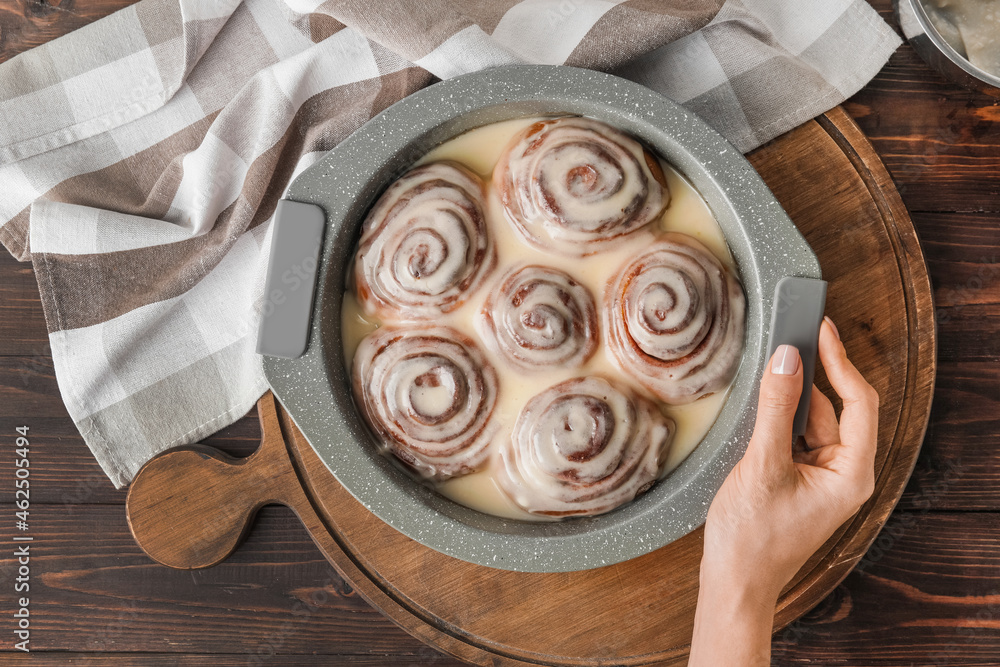 Female hand with tasty cinnamon rolls in baking dish, top view