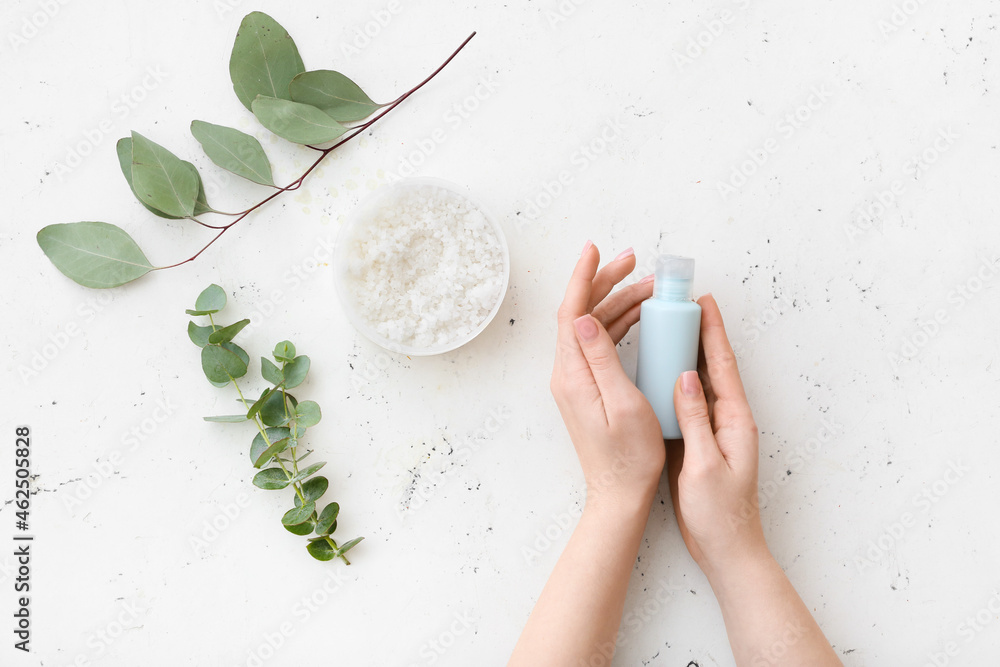 Female hands with bottle of cosmetic product and sea salt on white background