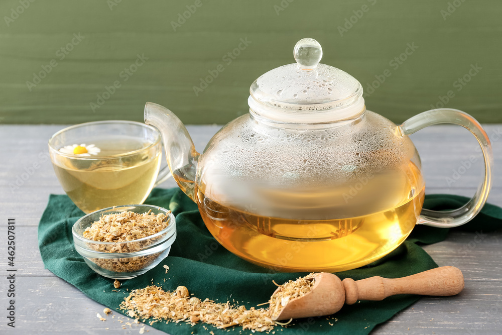 Teapot and cup of fresh chamomile tea on wooden table