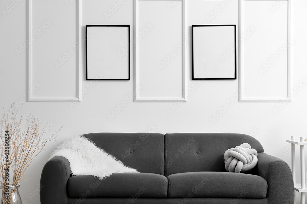 Living room with comfy sofa near light wall with blank poster frames