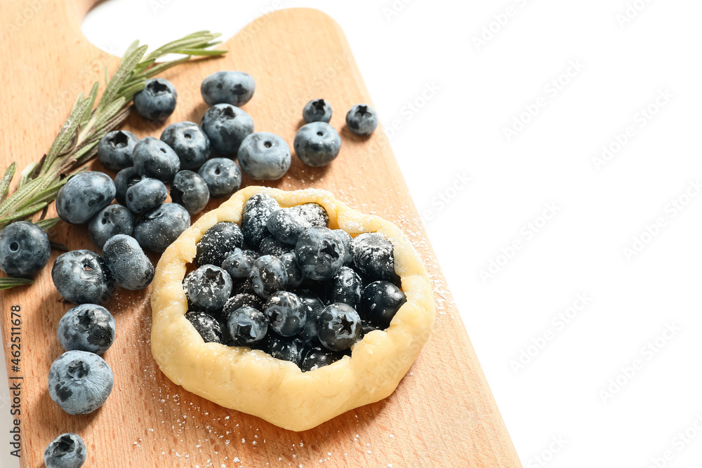 Board with raw blueberry galette and rosemary on white background