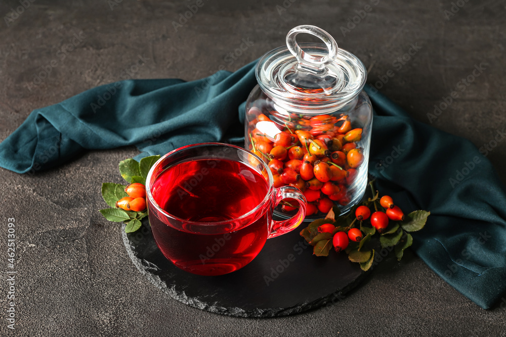 Glass cup of tasty rose hip tea and bowl with berries on table