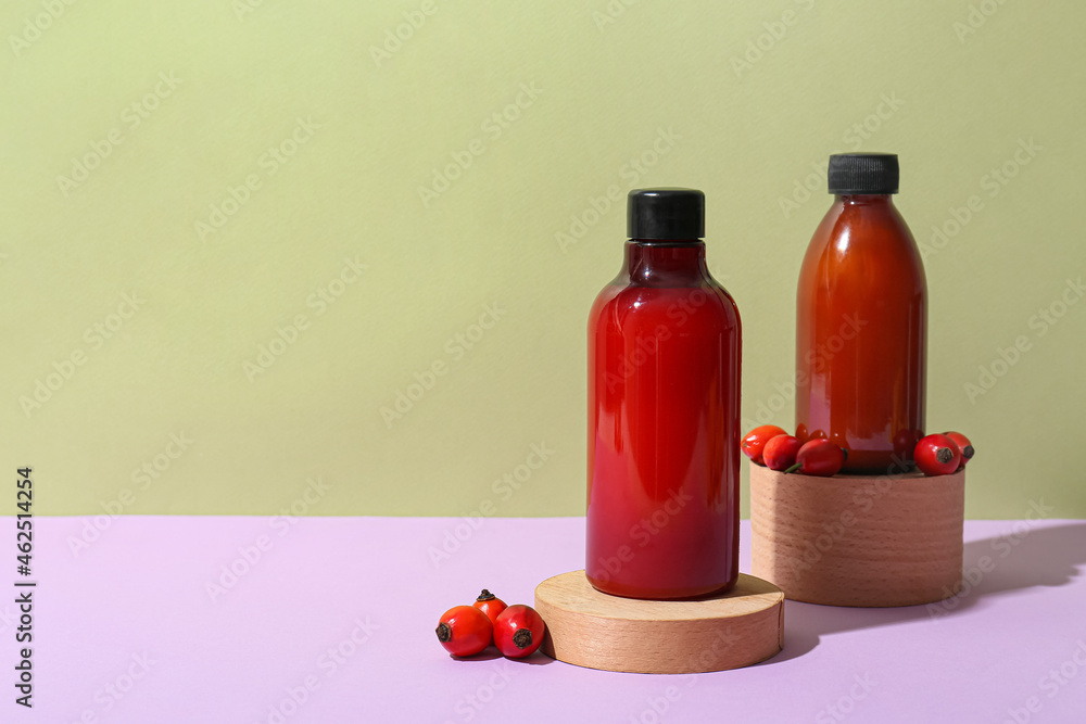 Bottles of cosmetic products and rose hip berries on color background