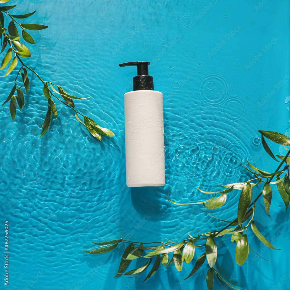 Bottle of cosmetic product and plant branches in water on color background