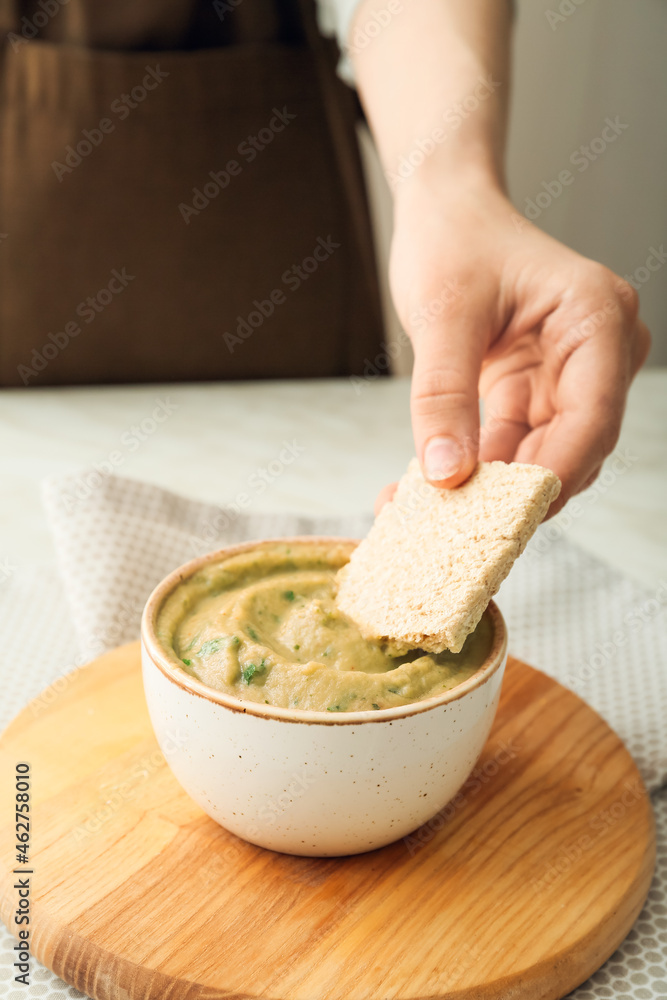 Man eating tasty baba ghanoush with cracker at table, closeup