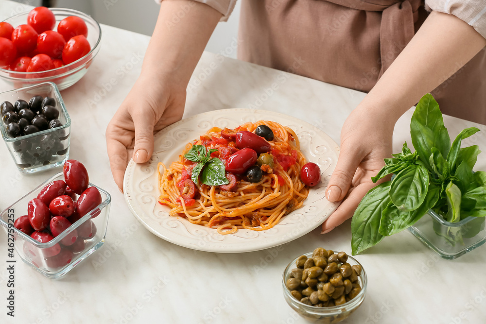 厨房桌子旁的女人拿着一盘美味的Pasta Puttanesca，特写镜头