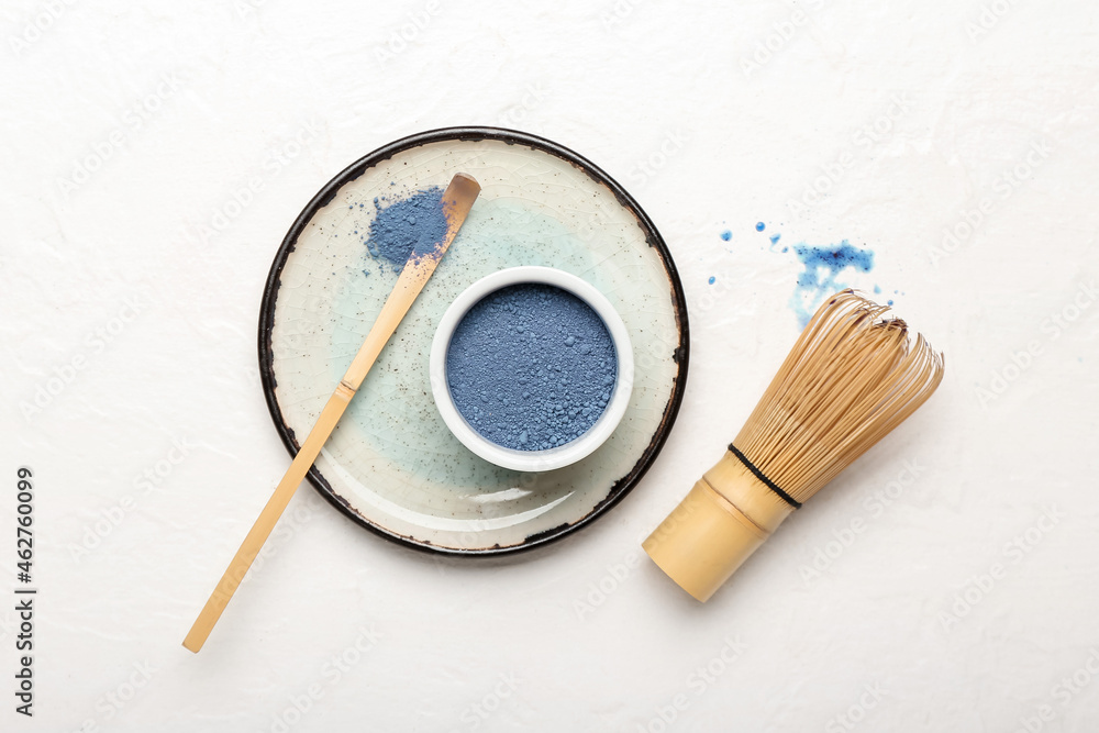 Bowl of powdered blue matcha tea, chashaku and chasen on light background