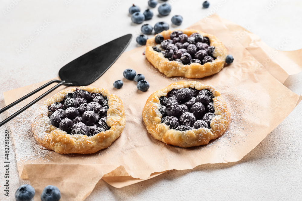 Parchment with tasty blueberry galettes on light background