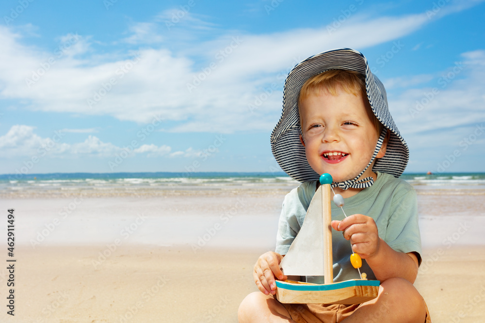 Boy play hold sail boat yacht sitting on a beach