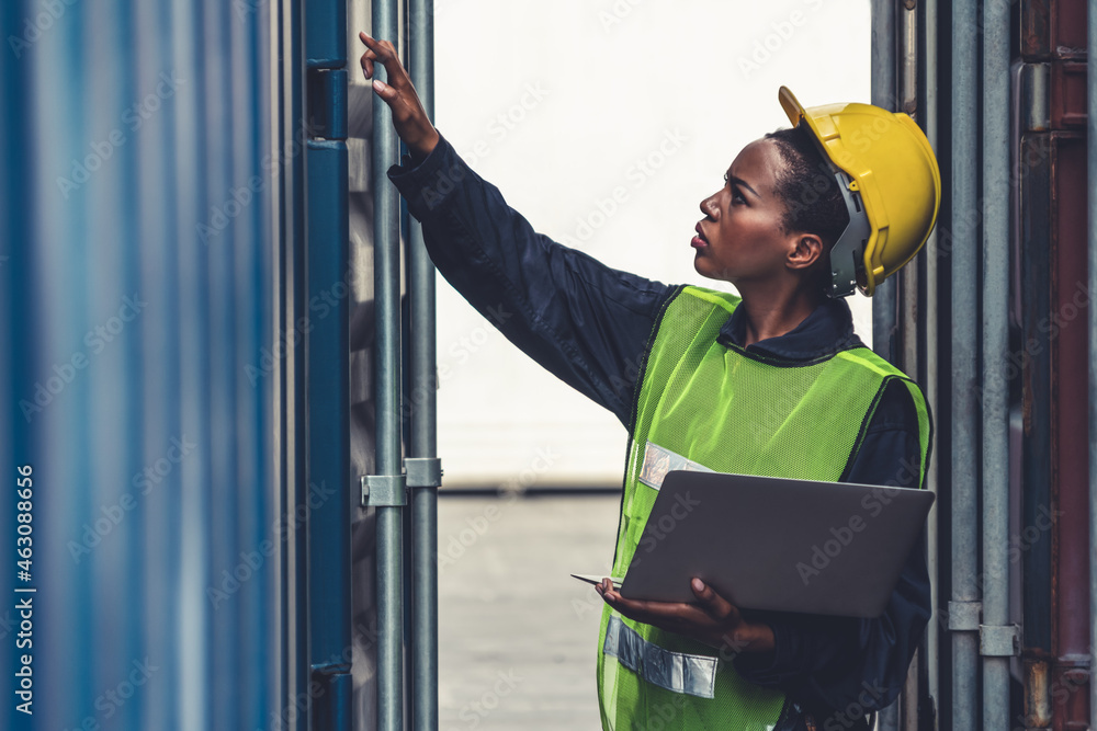 Young African American woman worker at overseas shipping container yard . Logistics supply chain man