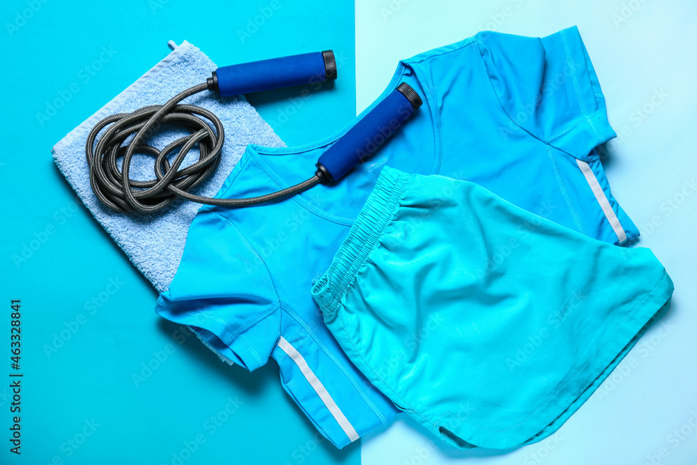 Sportswear, skipping rope and towel on color background