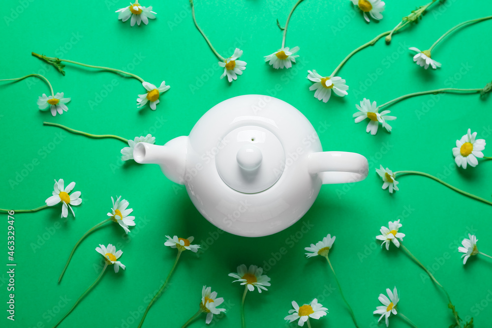 Teapot and chamomile flowers on green background