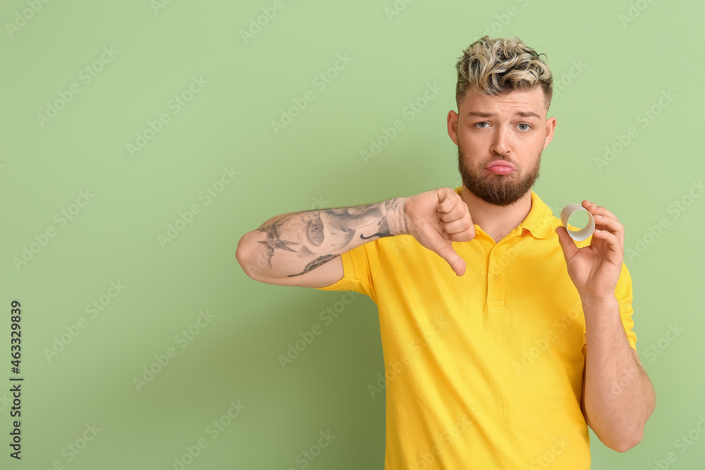 Sad young man out of toilet paper on color background