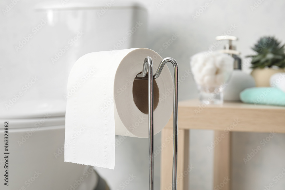 Holder with toilet paper roll in light restroom, closeup