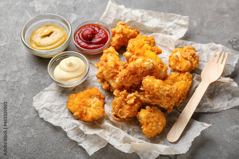 Parchment with tasty fried popcorn chicken and sauces on grey background