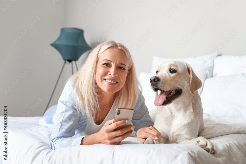 成熟的女人和可爱的拉布拉多犬在卧室里用手机