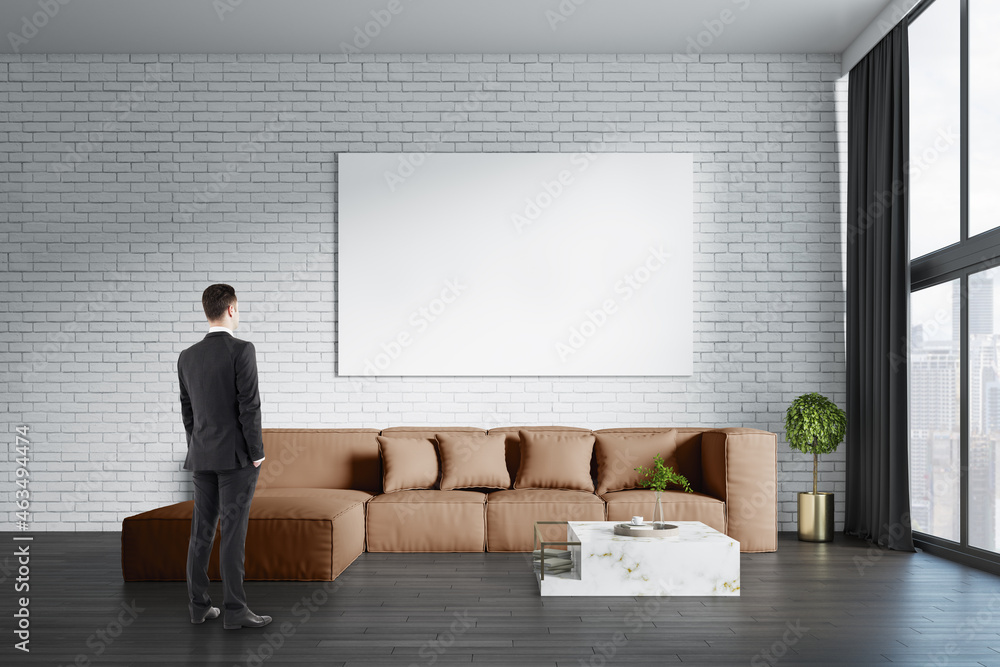 Young european businessman standing in modern living room interior with big couch, empty white mock 