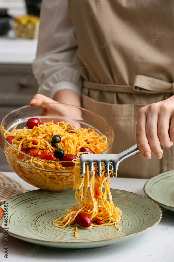 Woman preparing tasty Pasta Puttanesca at table in kitchen, closeup