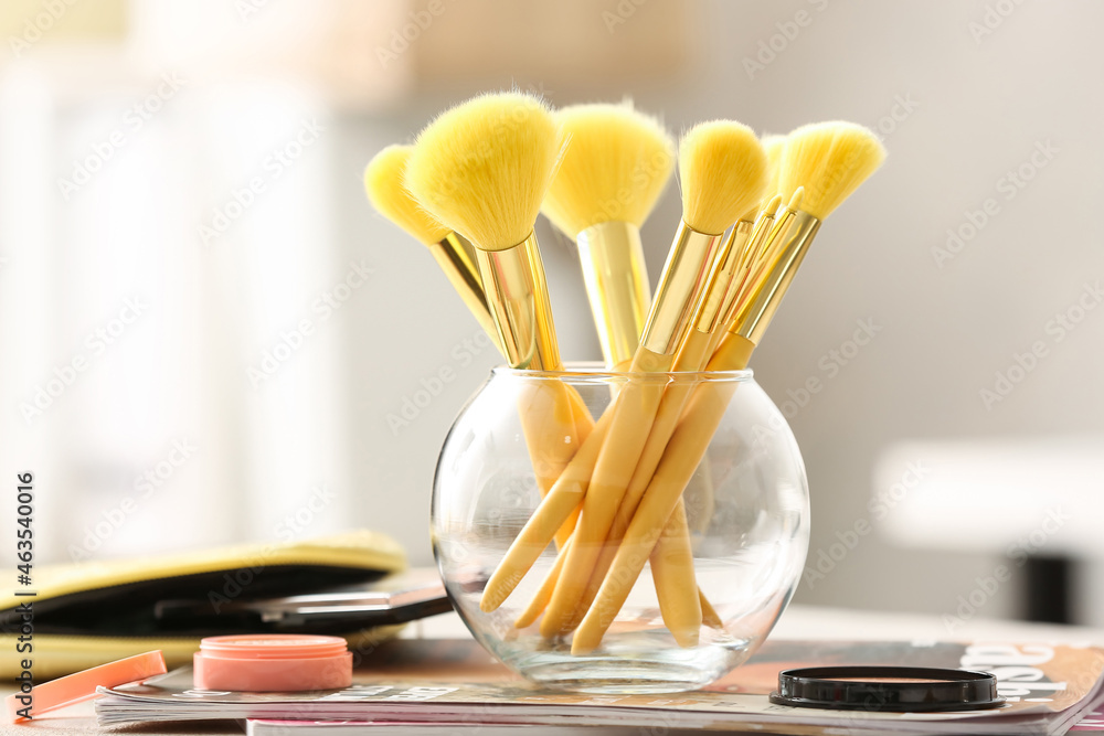 Glass with set of stylish makeup brushes on table