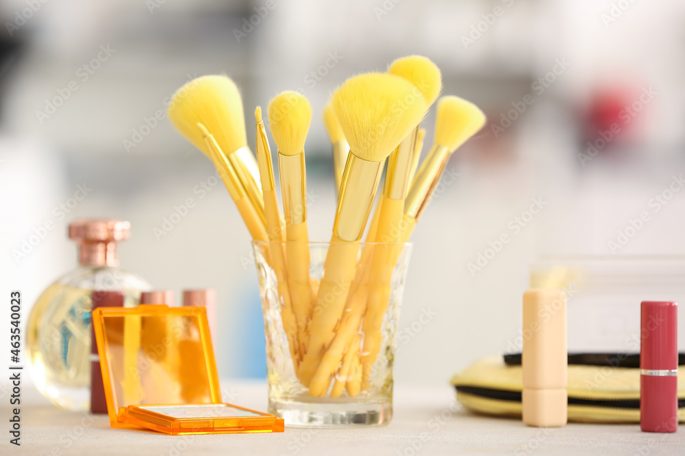 Glass with set of stylish makeup brushes on table