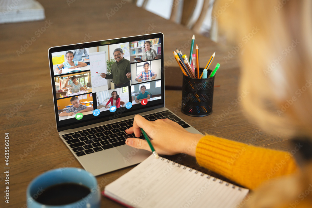 Caucasian woman using laptop for video call, with smiling diverse high school pupils on screen