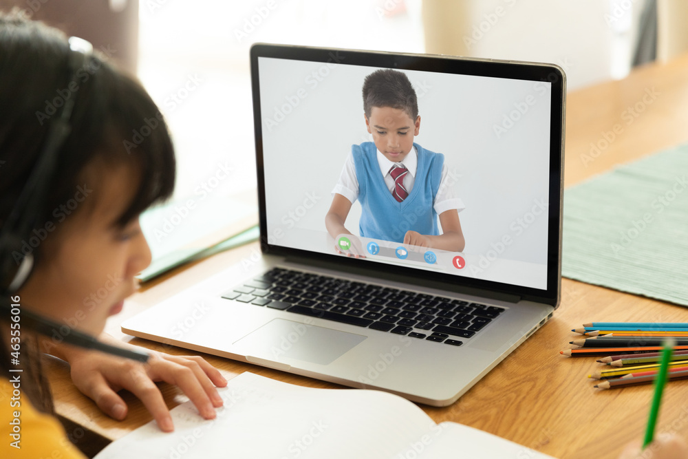 Asian girl using laptop for video call, with elementary school pupil on screen