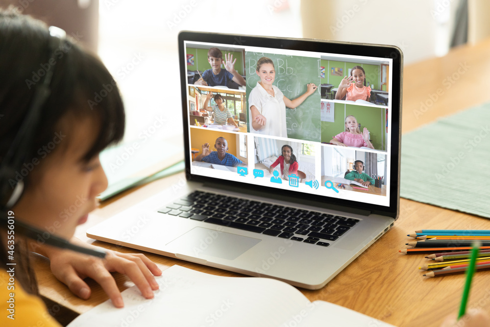 Asian girl using laptop for video call, with smiling diverse elementary school pupils on screen