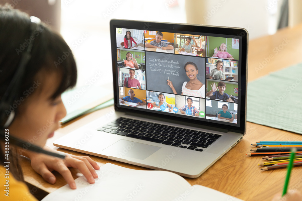 Asian girl using laptop for video call, with smiling diverse elementary school pupils on screen