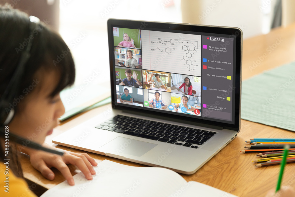 Asian girl using laptop for video call, with smiling diverse elementary school pupils on screen