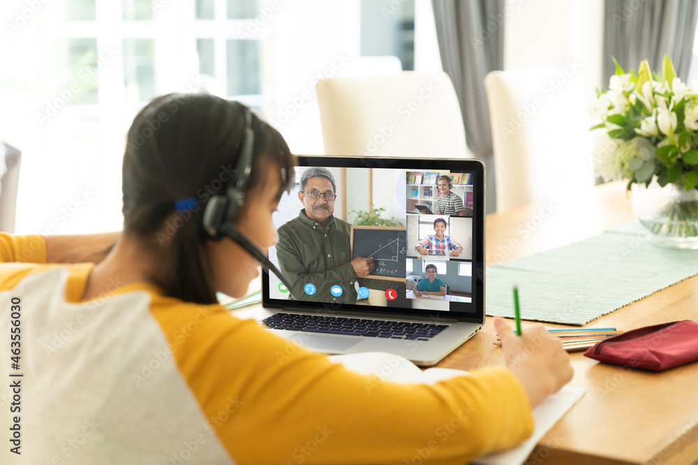 Asian girl using laptop for video call, with smiling diverse high school pupils on screen