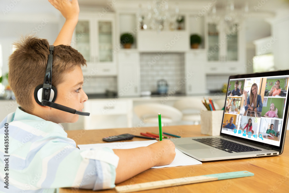 Caucasian boy raising hand for video call, with smiling diverse elementary school pupils on screen