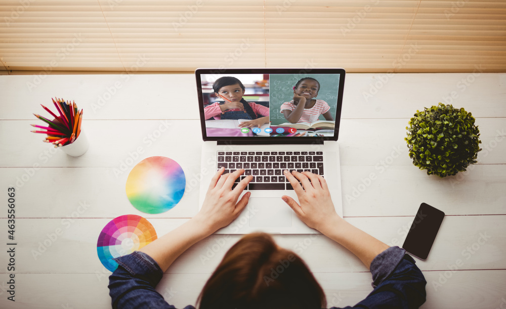 Caucasian woman using laptop for video call, with smiling diverse elementary school pupils on screen