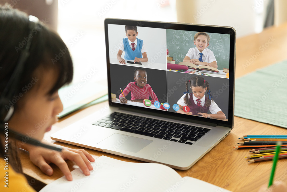 Asian girl using laptop for video call, with smiling diverse elementary school pupils on screen