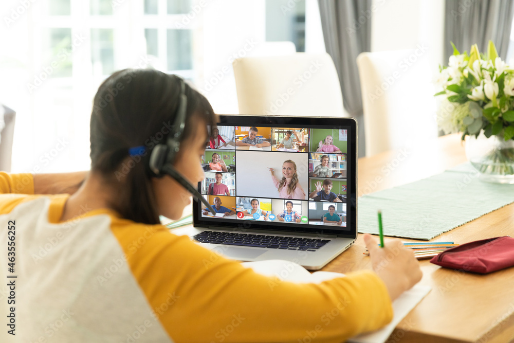 Asian girl using laptop for video call, with smiling diverse elementary school pupils on screen