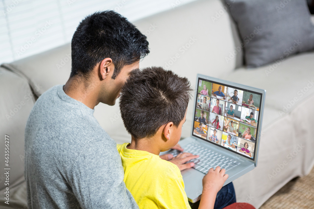 Biracial boy with father using laptop for video call, with elementary school pupils on screen