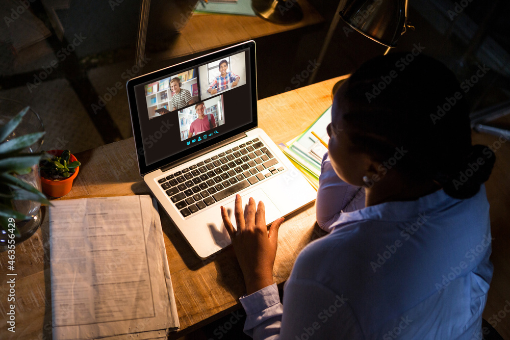 African american woman using laptop for video call, with diverse high school pupils on screen