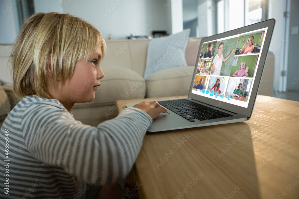 Caucasian boy using laptop for video call, with smiling diverse elementary school pupils on screen