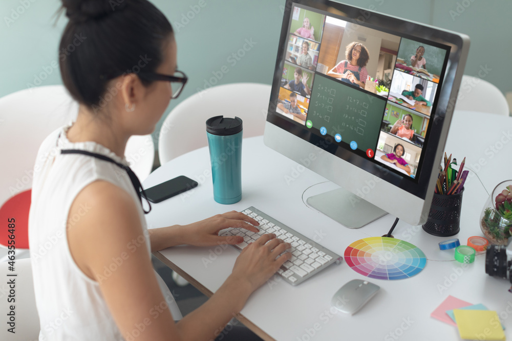 Asian girl using laptop for video call, with smiling diverse elementary school pupils on screen