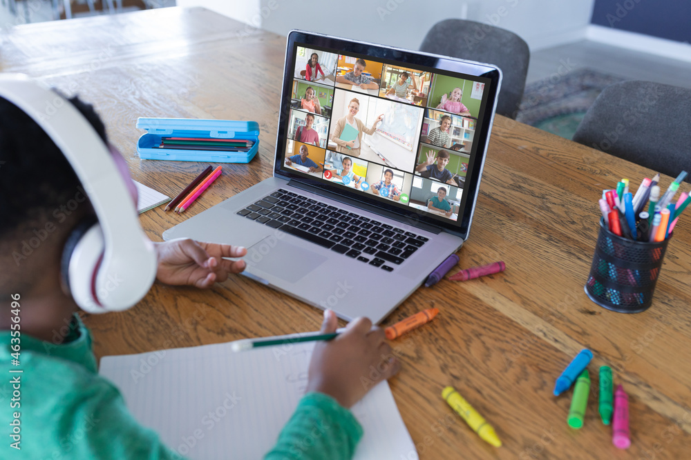 African american boy using laptop for video call, with diverse elementary school pupils on screen