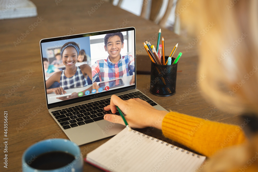 Caucasian woman using laptop for video call, with smiling diverse high school pupils on screen