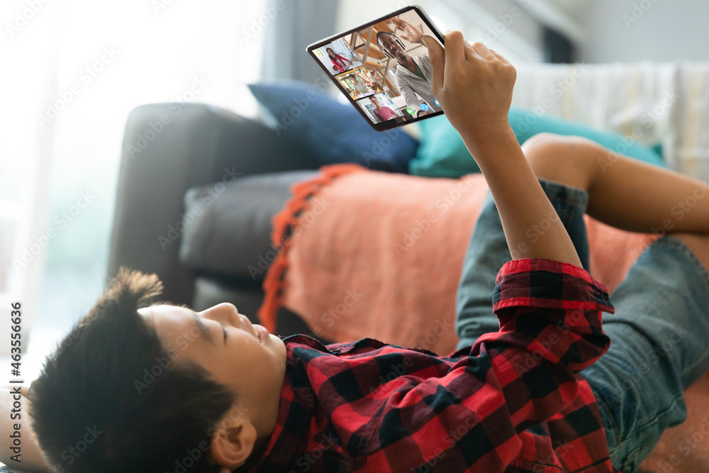 Asian boy using tablet for video call, with smiling diverse high school pupils on screen