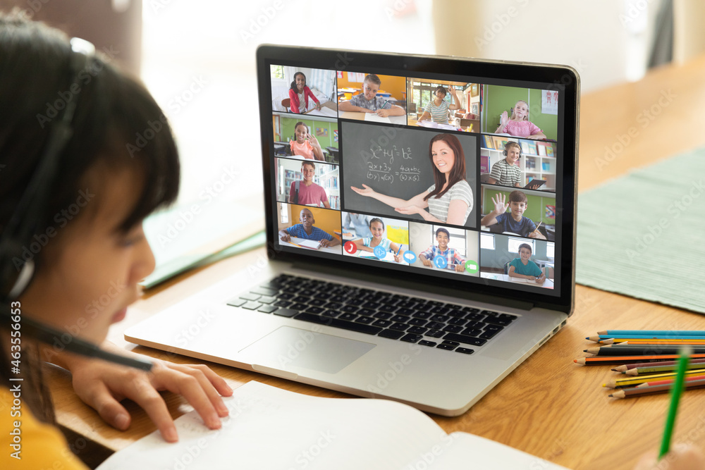 Asian girl using laptop for video call, with smiling diverse elementary school pupils on screen