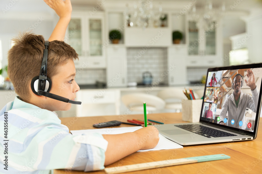 Caucasian boy raising hand for video call, with smiling diverse high school pupils on screen